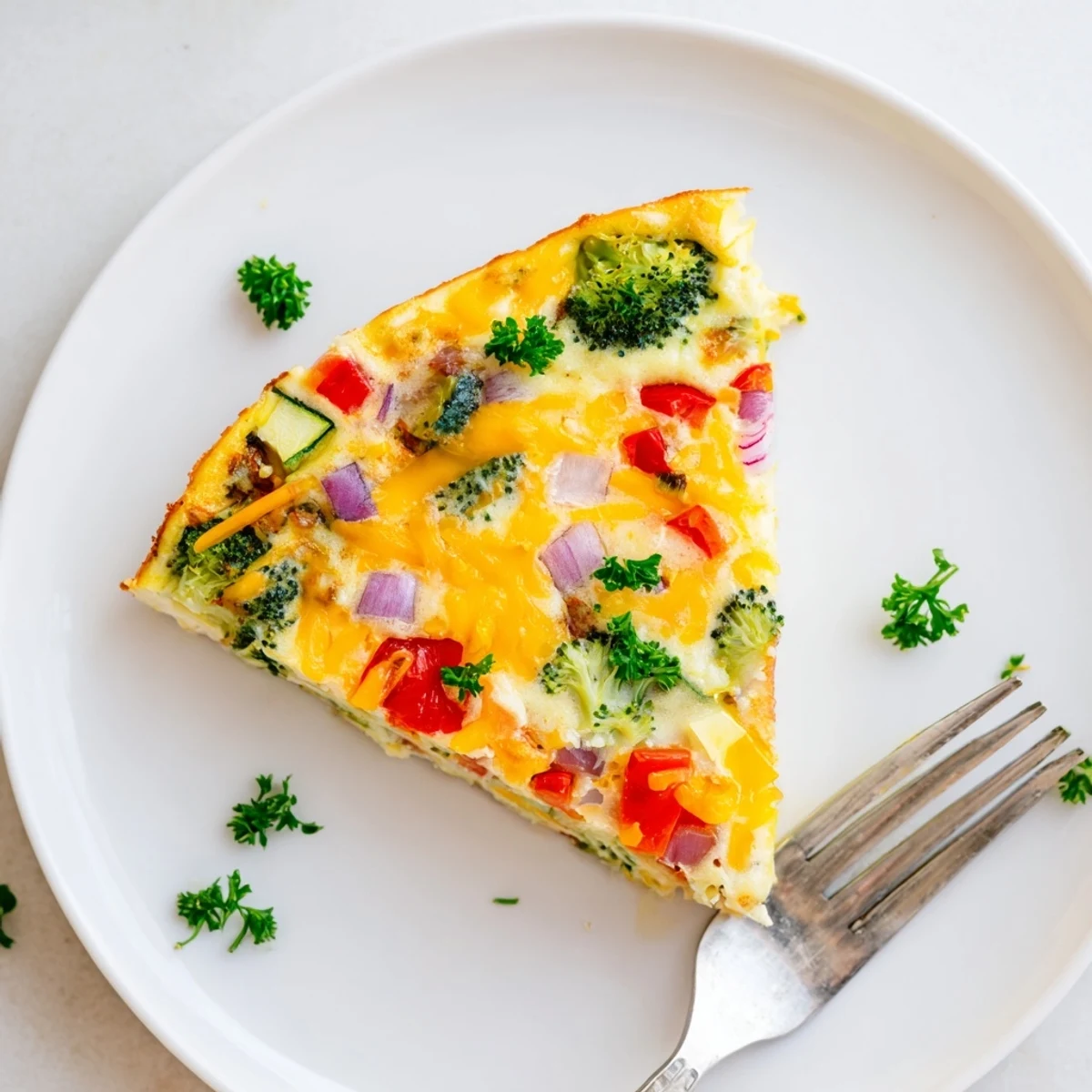 A golden Vegetable Frittata slice served on a white plate, garnished with parsley and a side of mixed greens for a light lunch.  