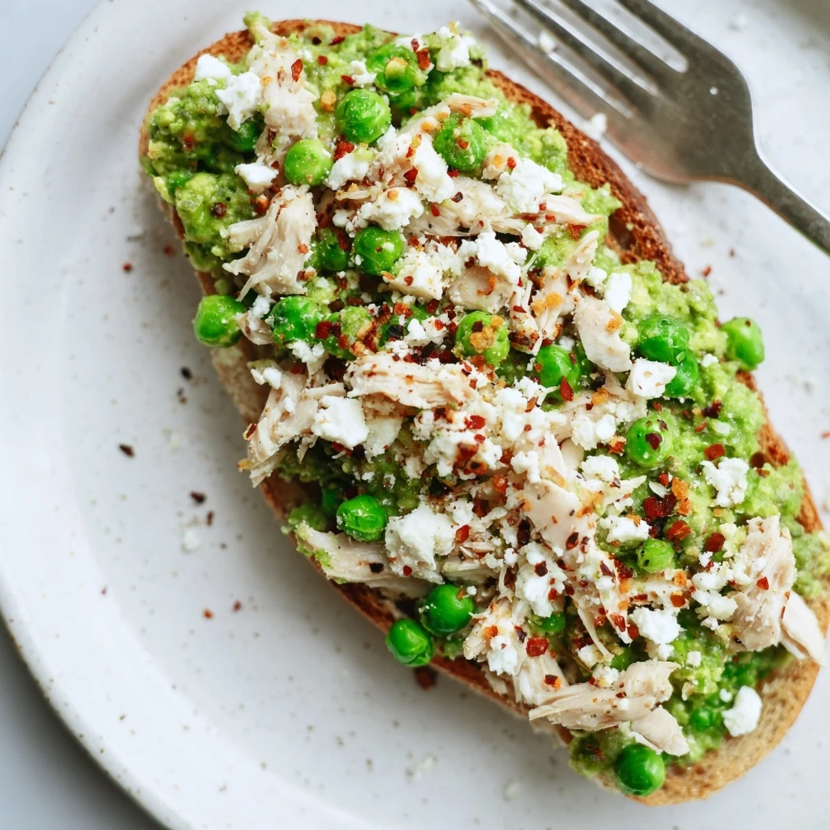 Close-up of Smashed Pea & Chicken Toast on rustic sourdough, showing creamy green pea mash with tender shredded chicken and a sprinkle of chili flakes.