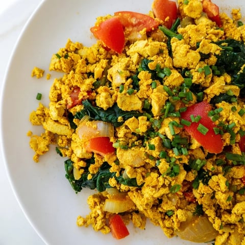 A vibrant plate of tofu scramble with diced red bell pepper, spinach, and turmeric-spiced crumbles, served warm for a hearty breakfast.