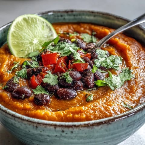 Vibrant Sweet Potato and Black Bean Soup garnished with cilantro and lime wedges in a rustic bowl. 