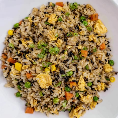 A close-up of savory black garlic fried rice topped with scallions and a sunny-side-up egg.  