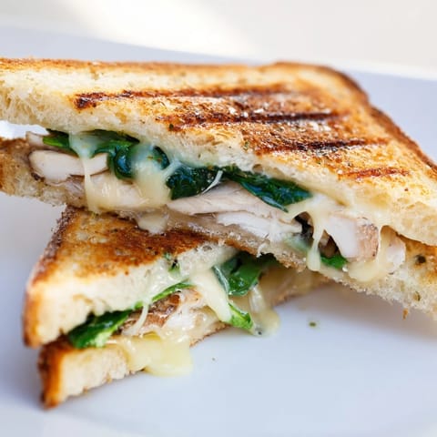A close-up of a Grilled Chicken Spinach Panini, showcasing melty cheese and vibrant spinach on crusty, buttery bread.  