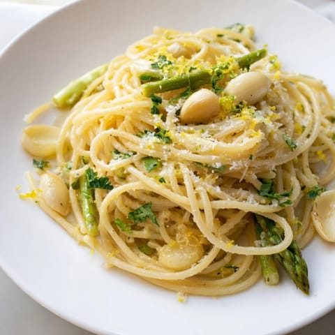 Freshly prepared Roasted Garlic & Asparagus Pasta steaming in a skillet, garnished with grated Parmesan cheese, lemon zest, and chopped parsley for a vibrant spring meal.  