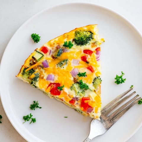 A golden Vegetable Frittata slice served on a white plate, garnished with parsley and a side of mixed greens for a light lunch.  