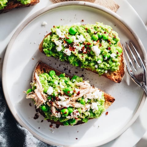 A plated Smashed Pea & Chicken Toast garnished with fresh mint and crumbled feta, served with a glass of crisp white wine.