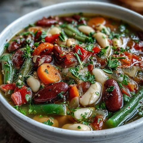 A vibrant bowl of Three-Bean Salad Soup with kidney and cannellini beans, cherry tomatoes, and red bell peppers.