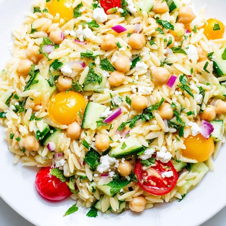 Overhead shot of a colorful Lemony Chickpea Orzo Salad, a Mediterranean-inspired dish with glistening pasta, chickpeas, fresh herbs, and vegetables, served as a perfect light meal for picnics or potlucks.