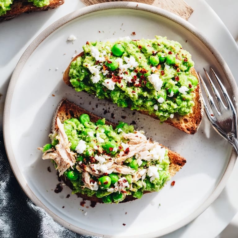 A plated Smashed Pea & Chicken Toast garnished with fresh mint and crumbled feta, served with a glass of crisp white wine.