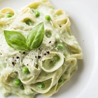 Creamy Green Pea Alfredo pasta twirled on a fork, with vibrant green sauce and fresh basil garnish.  
